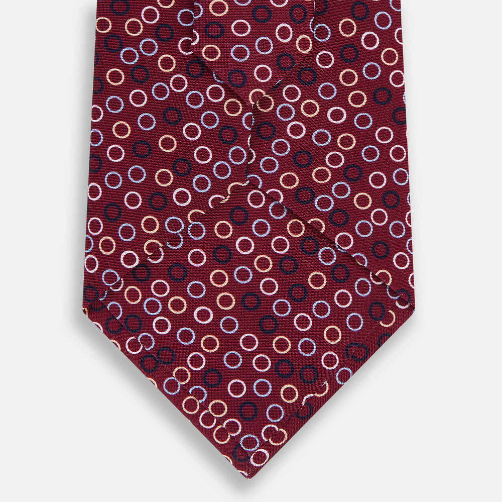 The Turnbull & Asser Pink and Navy Circle Burgundy Silk Tie features a rolled burgundy silk design with small, evenly spaced white, pink, and light blue circle patterns.