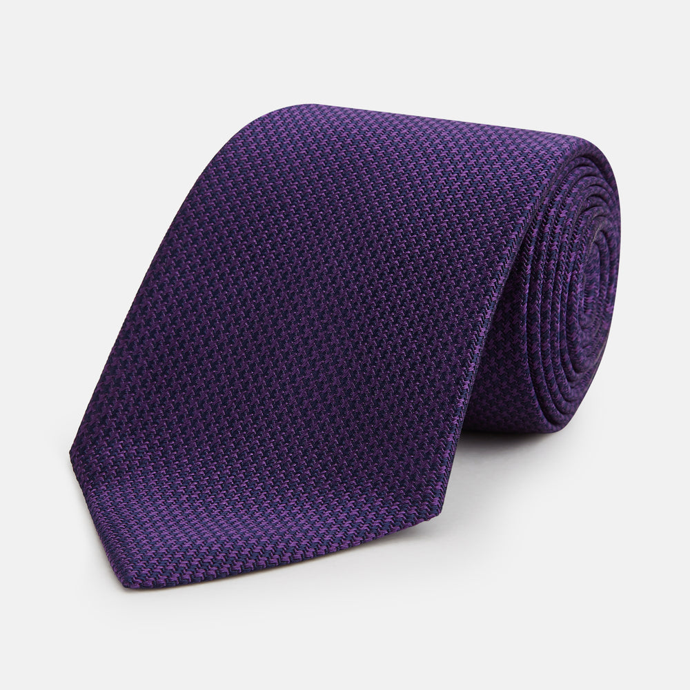The HOUNDSTOOTH NAVY PLUM TIE by Turnbull & Asser, featuring a textured pattern, is showcased rolled up against a plain white background—an essential accessory.