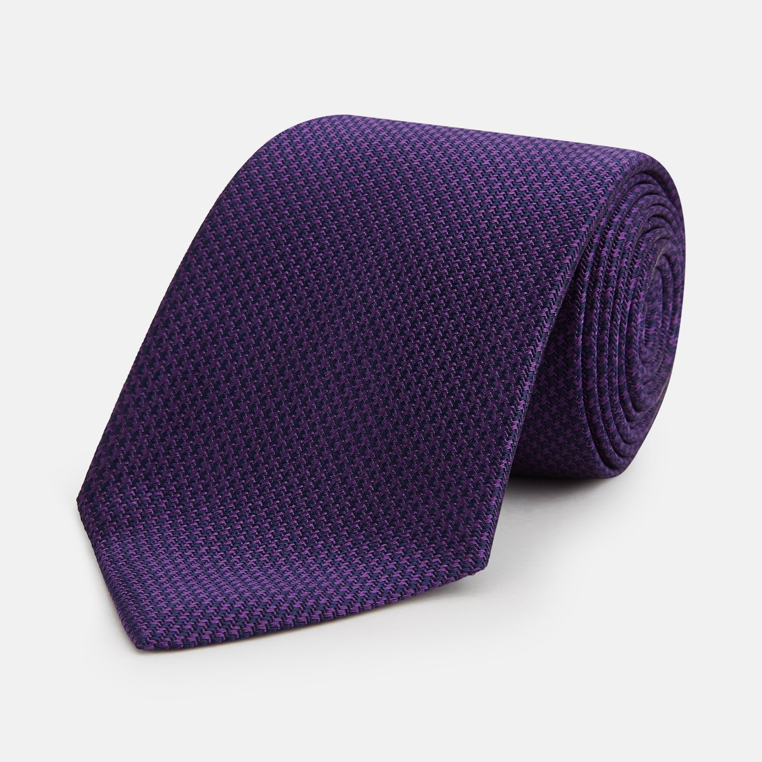 View 1 of product The HOUNDSTOOTH NAVY PLUM TIE by Turnbull & Asser, featuring a textured pattern, is showcased rolled up against a plain white background—an essential accessory.