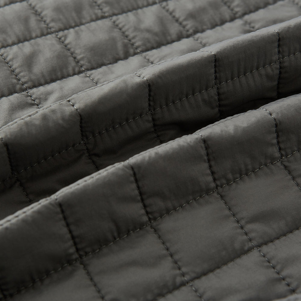 The Turnbull & Asser Shadow Grey Double-Breasted Quilted Gilet features a sleeveless design, asymmetrical collar, side zip pockets, slanted chest pocket, grid pattern, and modern black buttons—perfect for layered dressing.