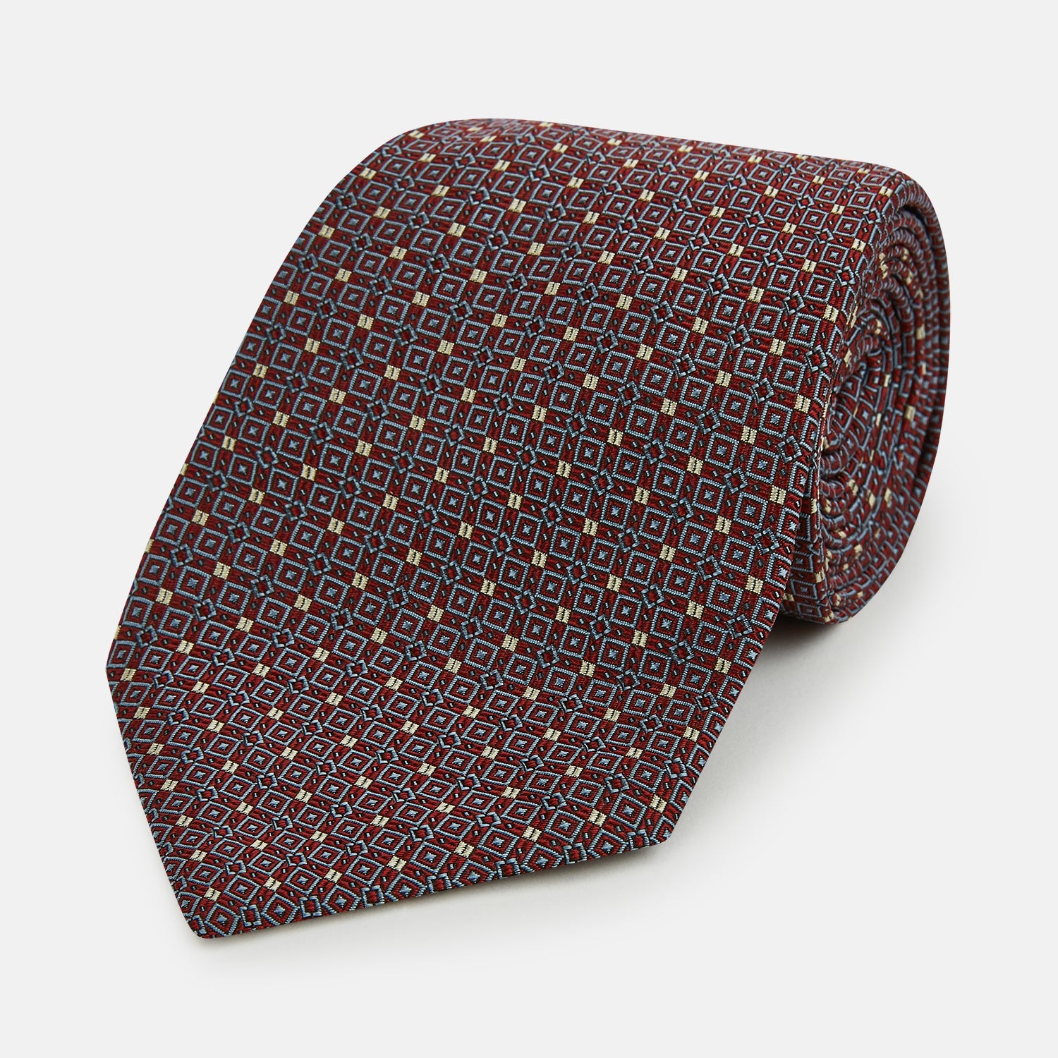 View 1 of product The Turnbull & Asser Burgundy Geometric Silk Tie, crafted in Britain, features a repeating pattern of light blue and white squares and diamonds. The neatly rolled tie is shown against a plain white background.