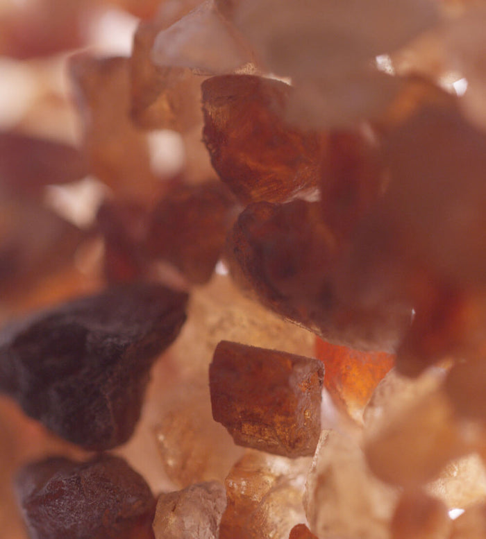 Close-up of rough, irregularly shaped crystals in shades of amber, orange, brown, and beige, with a soft focus creating a warm and textured appearance.