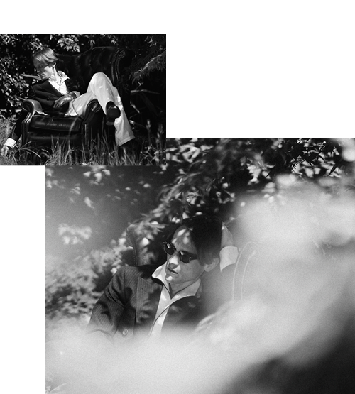 Black and white photos of a person in sunglasses and a suit, lounging on an outdoor armchair, partially obscured by plants and sunlight. The top image shows a wider view; the bottom is a closer shot.