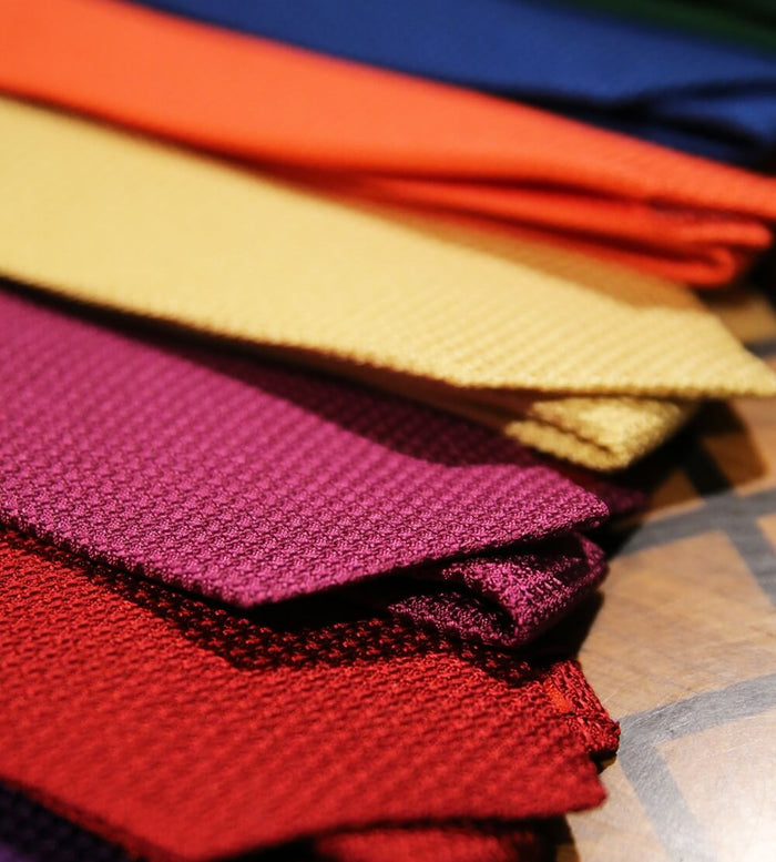 A close-up of neatly arranged textured fabric swatches in vibrant colors, including red, yellow, orange, purple, and blue, displayed on a wooden surface.