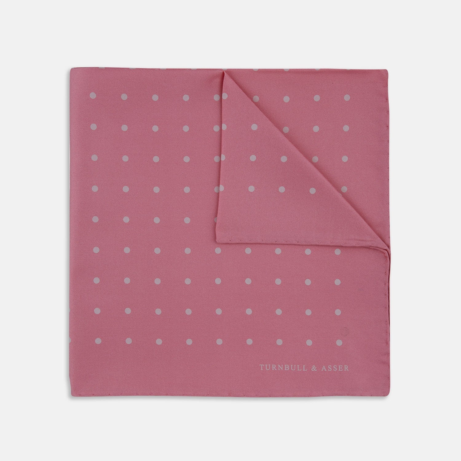 View 1 of product The Rose and White Spot Silk Pocket Square by Turnbull & Asser features rose pink silk with white polka dots and Turnbull & Asser branding in the corner—a refined accessory for any navy suit collection.
