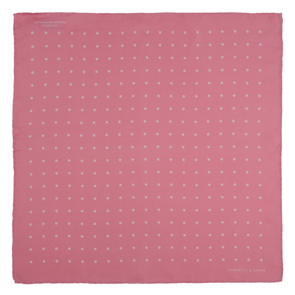 The Rose and White Spot Silk Pocket Square by Turnbull & Asser features rose pink silk with white polka dots and Turnbull & Asser branding in the corner—a refined accessory for any navy suit collection.
