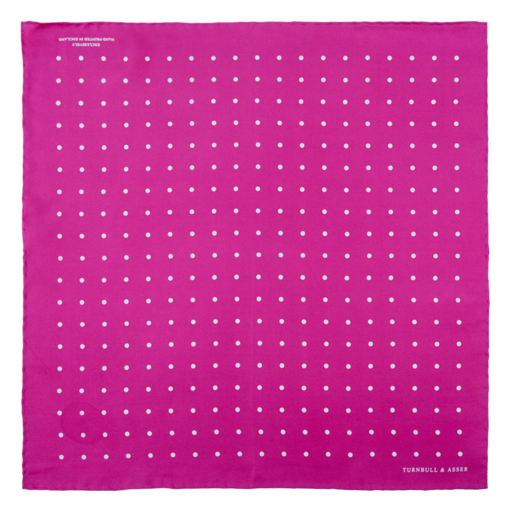 The Fuchsia Spot Silk Pocket Square by Turnbull & Asser features bright fuchsia silk with evenly spaced white spots and the brand’s name in one corner. A classic accessory, it is shown with one corner folded over.