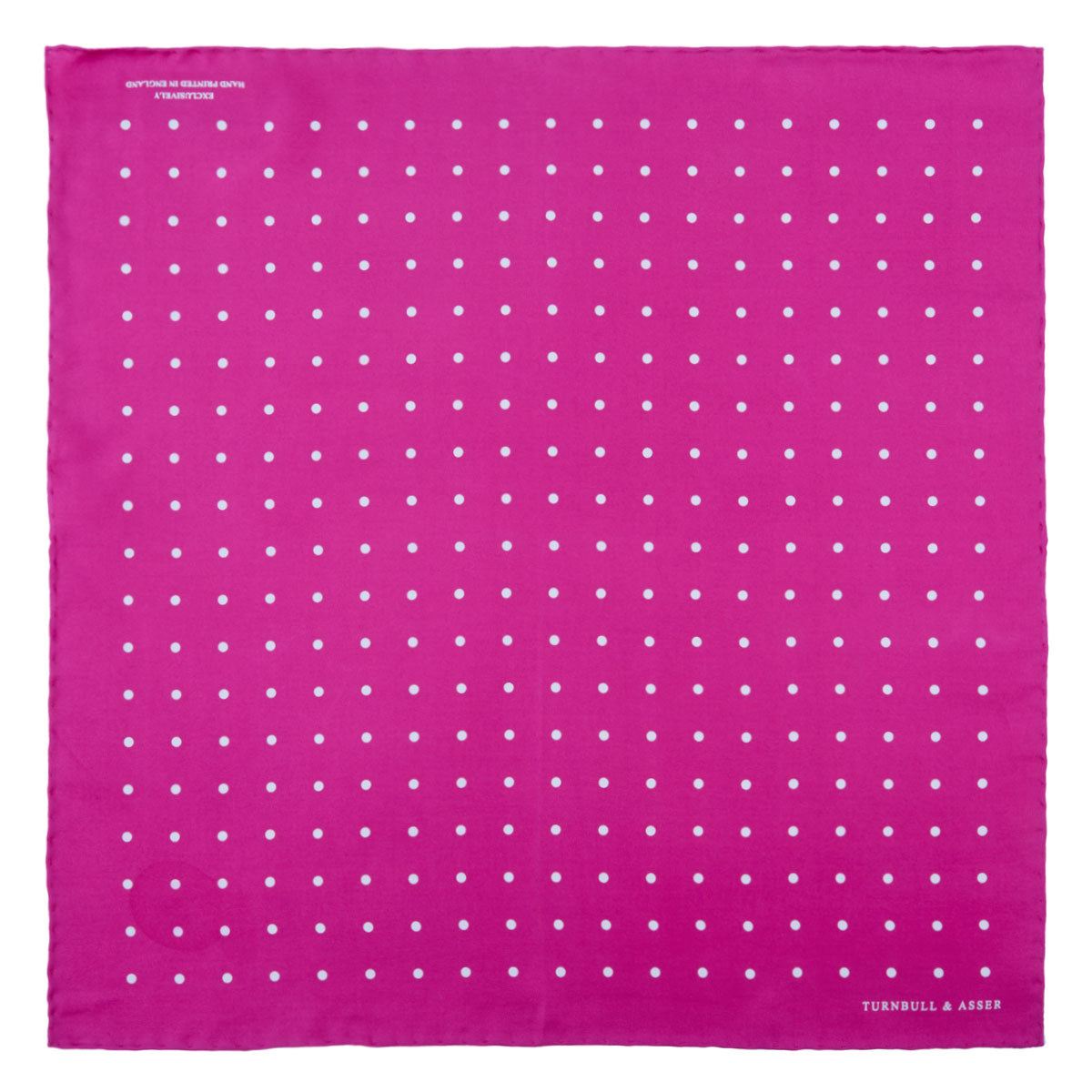 View 2 of product The Fuchsia Spot Silk Pocket Square by Turnbull & Asser features bright fuchsia silk with evenly spaced white spots and the brand’s name in one corner. A classic accessory, it is shown with one corner folded over.