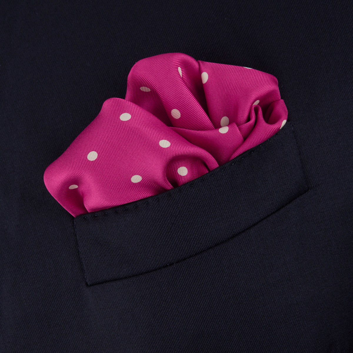 View 4 of product The Fuchsia Spot Silk Pocket Square by Turnbull & Asser features bright fuchsia silk with evenly spaced white spots and the brand’s name in one corner. A classic accessory, it is shown with one corner folded over.