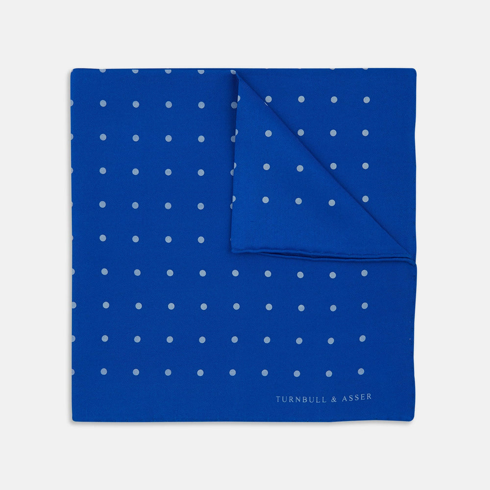 The Royal Blue Spot Silk Pocket Square by Turnbull & Asser features evenly spaced white polka dots and a branded corner, making it the perfect accessory to add flair to pinstripe suits.