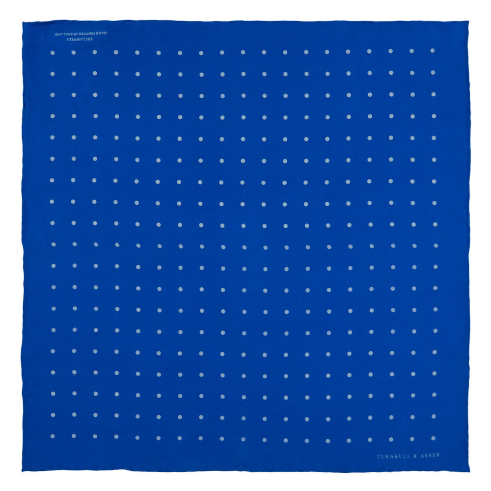 The Royal Blue Spot Silk Pocket Square by Turnbull & Asser features evenly spaced white polka dots and a branded corner, making it the perfect accessory to add flair to pinstripe suits.