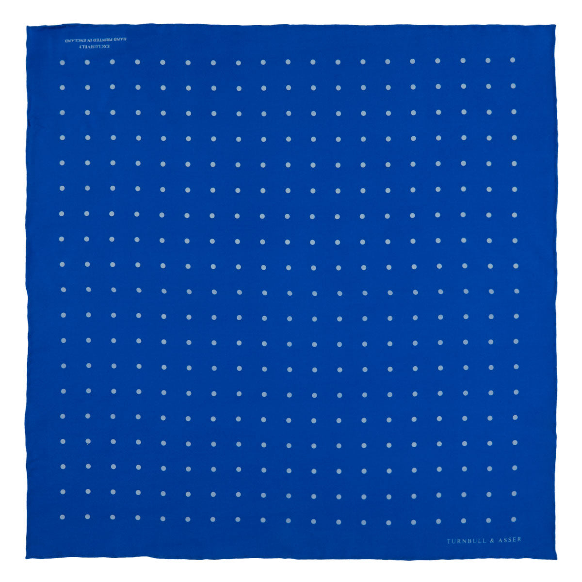 View 2 of product The Royal Blue Spot Silk Pocket Square by Turnbull & Asser features evenly spaced white polka dots and a branded corner, making it the perfect accessory to add flair to pinstripe suits.
