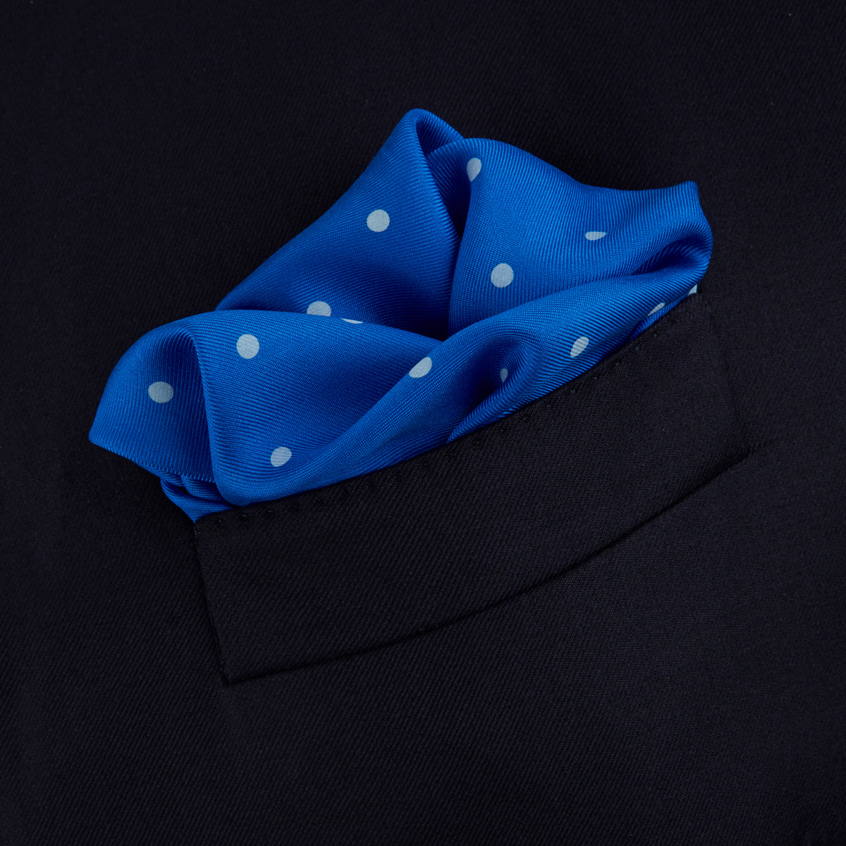 View 4 of product The Royal Blue Spot Silk Pocket Square by Turnbull & Asser features evenly spaced white polka dots and a branded corner, making it the perfect accessory to add flair to pinstripe suits.