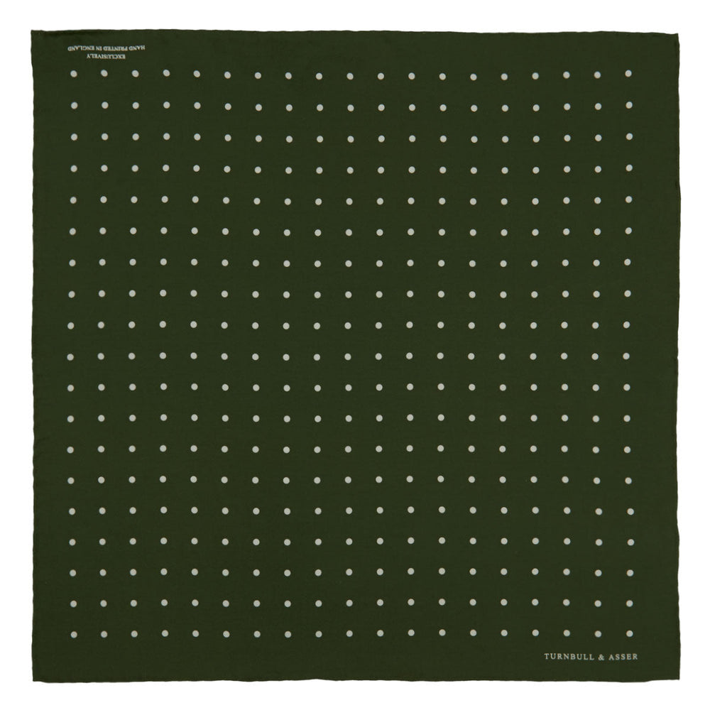 The Turnbull & Asser Olive Spot Silk Pocket Square features white polka dots, the brand’s logo in one corner, and a stylishly folded tip for a dapper finish.