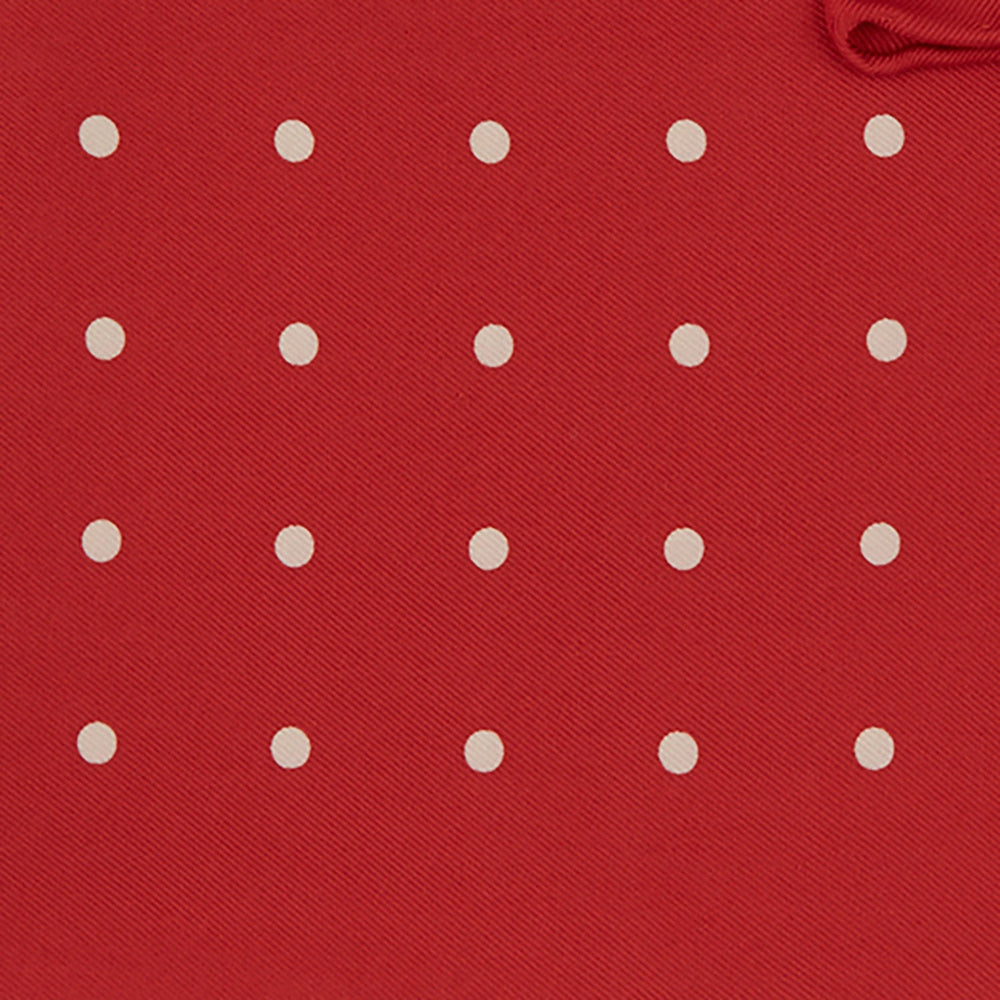 The Red and White Spot Silk Pocket Square by Turnbull & Asser features evenly spaced white polka dots on red silk with the brand's name printed in one corner. A folded edge reveals the reverse of this timeless pocket square.
