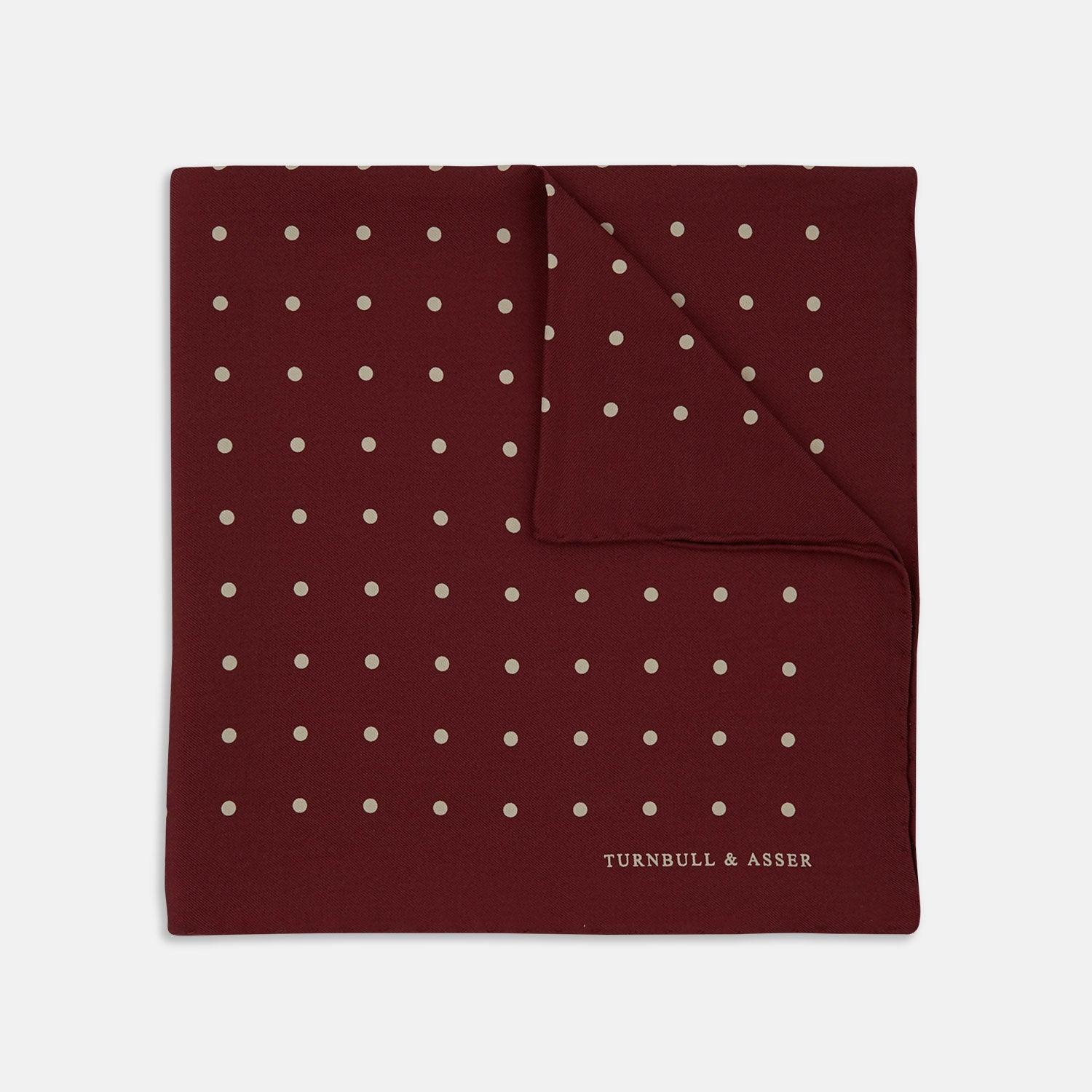 View 1 of product Add a touch of elegance with the Turnbull & Asser Burgundy Spot Silk Pocket Square, featuring white dots, a printed corner logo, and folded edging—a classic men’s accessory for any occasion.