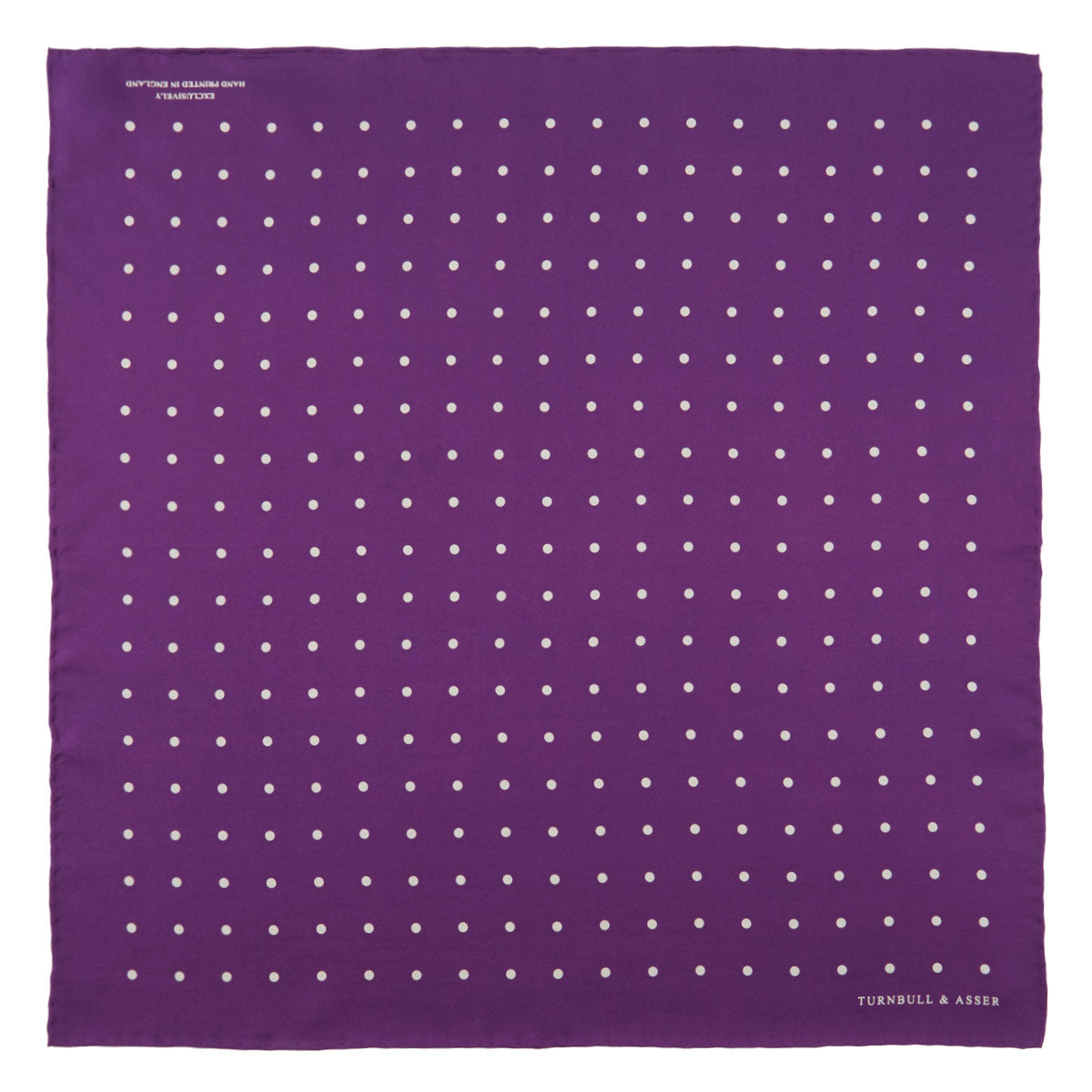 View 2 of product The Turnbull & Asser Purple Spot Silk Pocket Square features white polka dots and a small logo in the corner, with one corner folded over to showcase the underside.