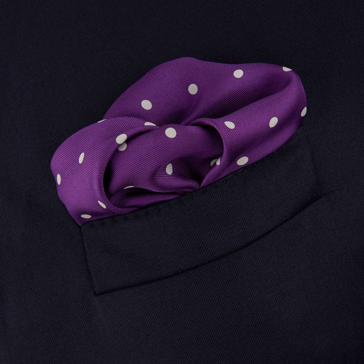 View 4 of product The Turnbull & Asser Purple Spot Silk Pocket Square features white polka dots and a small logo in the corner, with one corner folded over to showcase the underside.