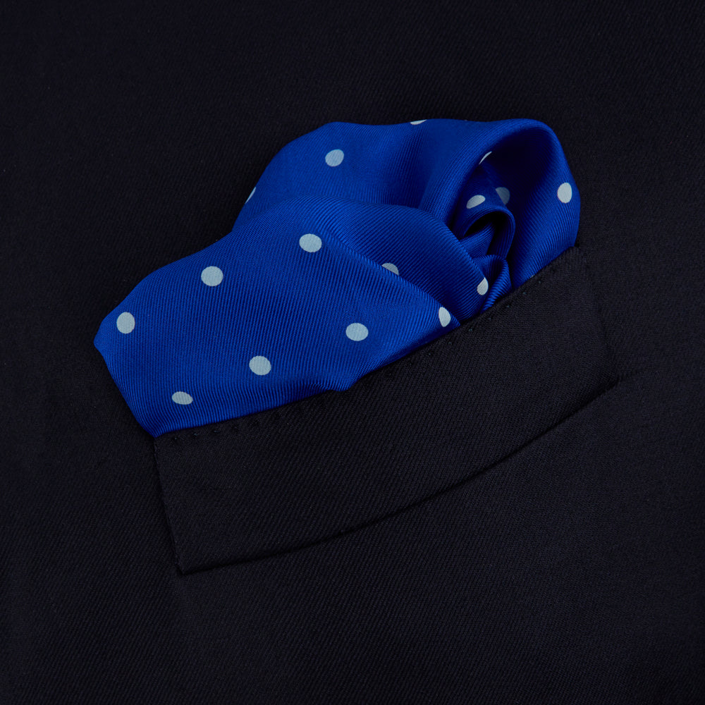 The Bright Blue Spot Silk Pocket Square by Turnbull & Asser features evenly spaced white polka dots and the brand's name printed in white in the bottom right corner, making it a stylish accessory for any suit.