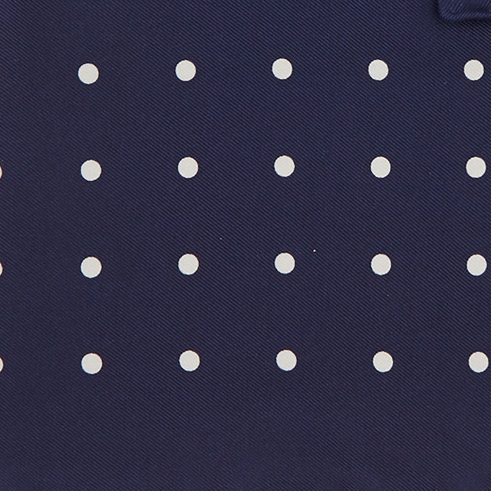 The Navy Spot Silk Pocket Square by Turnbull & Asser features a white polka dot pattern and is neatly folded at one corner, with the brand name printed in white on the lower right—perfect for pairing with pinstripe suits.