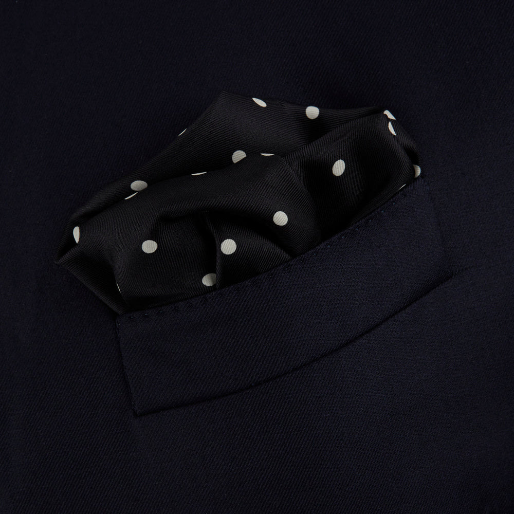 The Black Spot Silk Pocket Square by Turnbull & Asser features classic white polka dots on black silk, with the brand name printed in one corner and a stylish folded design.