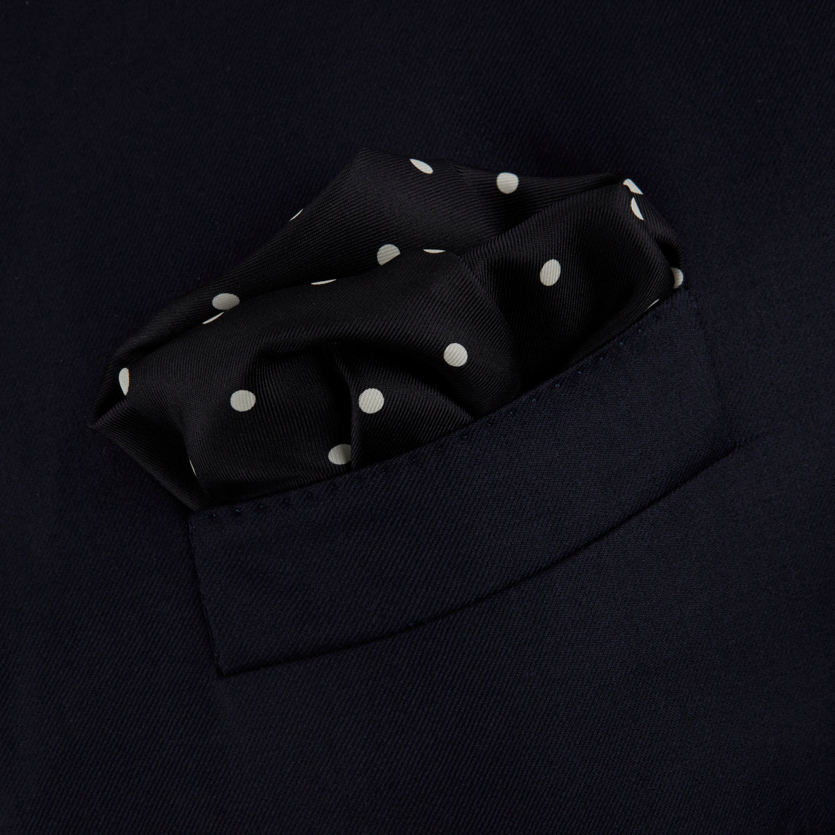 View 4 of product The Black Spot Silk Pocket Square by Turnbull & Asser features classic white polka dots on black silk, with the brand name printed in one corner and a stylish folded design.