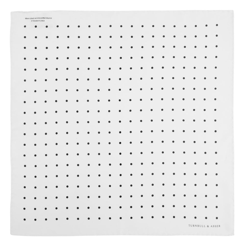 The Turnbull & Asser White and Black Spot Silk Pocket Square for men features evenly spaced black dots, a partial corner fold, and the brand name printed in black in the lower right corner.