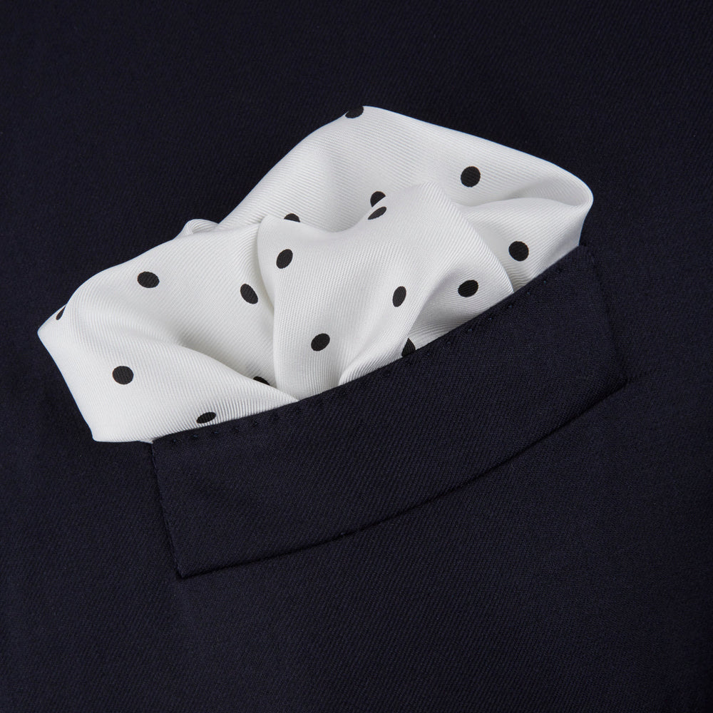 The Turnbull & Asser White and Black Spot Silk Pocket Square for men features evenly spaced black dots, a partial corner fold, and the brand name printed in black in the lower right corner.
