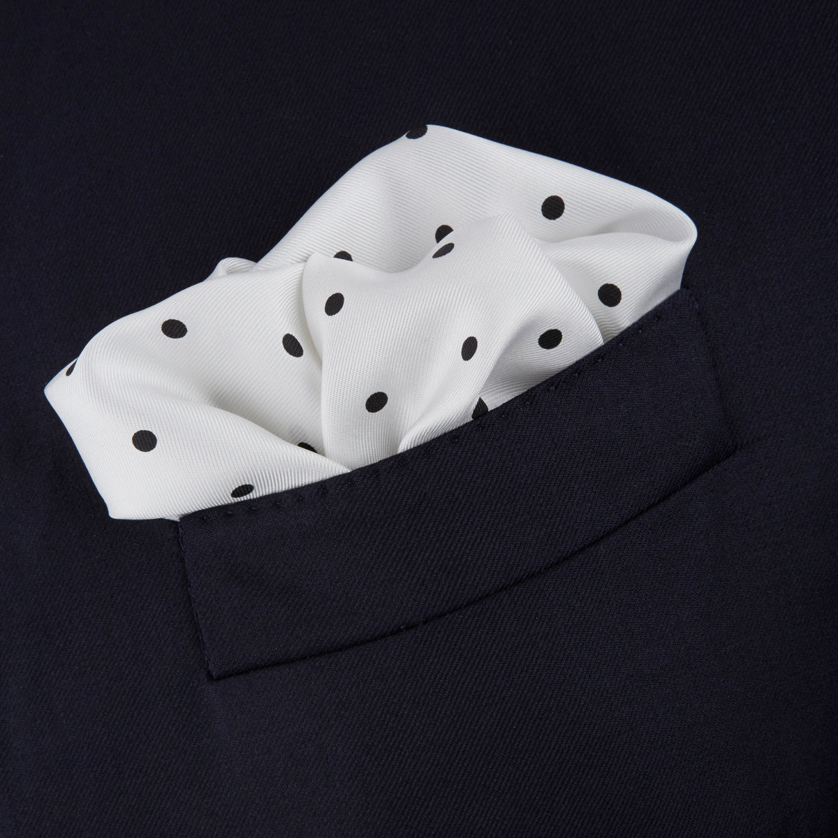 View 4 of product The Turnbull & Asser White and Black Spot Silk Pocket Square for men features evenly spaced black dots, a partial corner fold, and the brand name printed in black in the lower right corner.