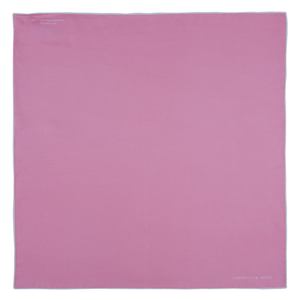 The Pink and White Piped Silk Pocket Square by Turnbull & Asser, featuring the brand’s name in white on one corner, is elegantly folded and set against a plain white background.