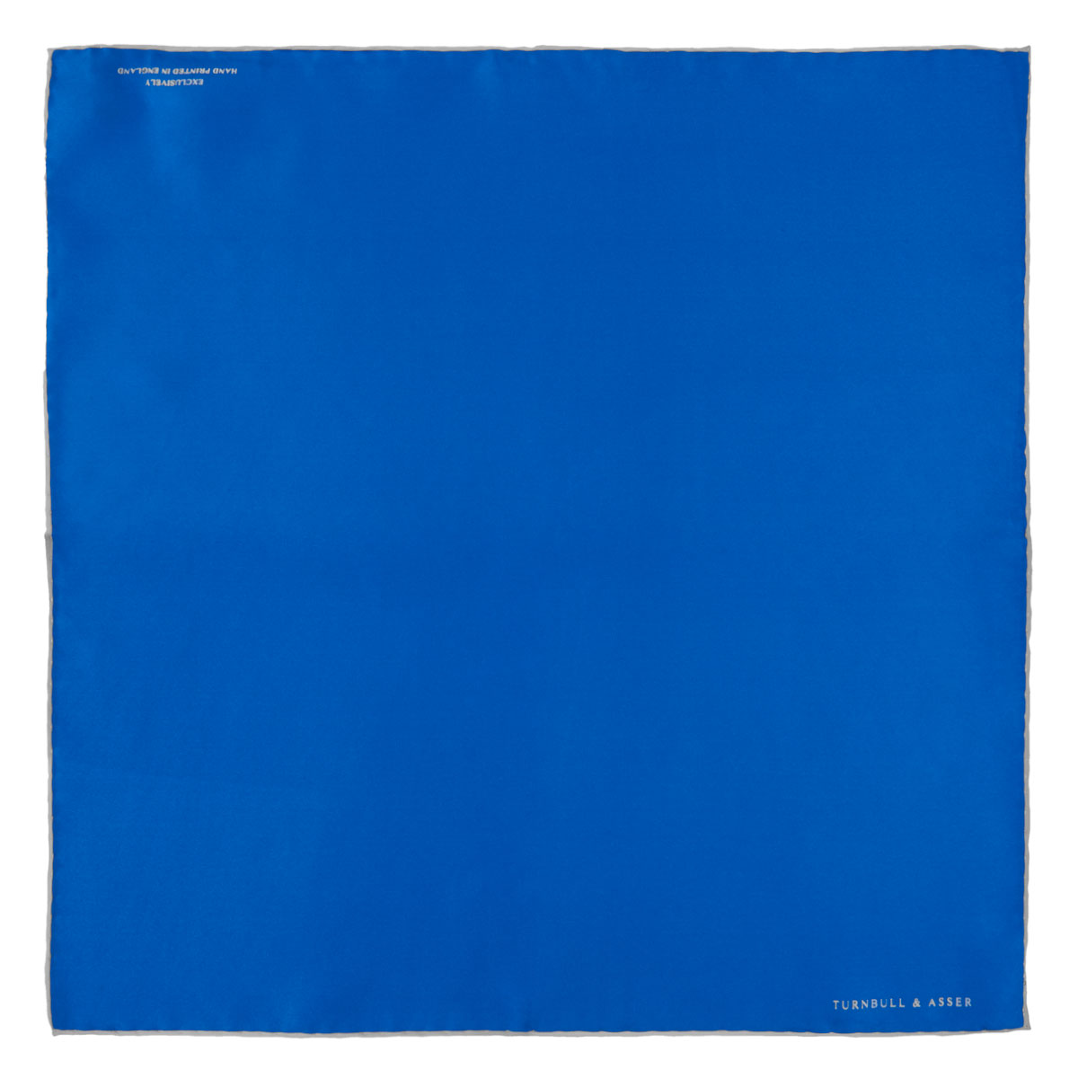 View 2 of product The Royal Blue Piped Silk Pocket Square by Turnbull & Asser features a vibrant blue hue, subtle stitched border, and the brand name printed in white in the lower right corner.