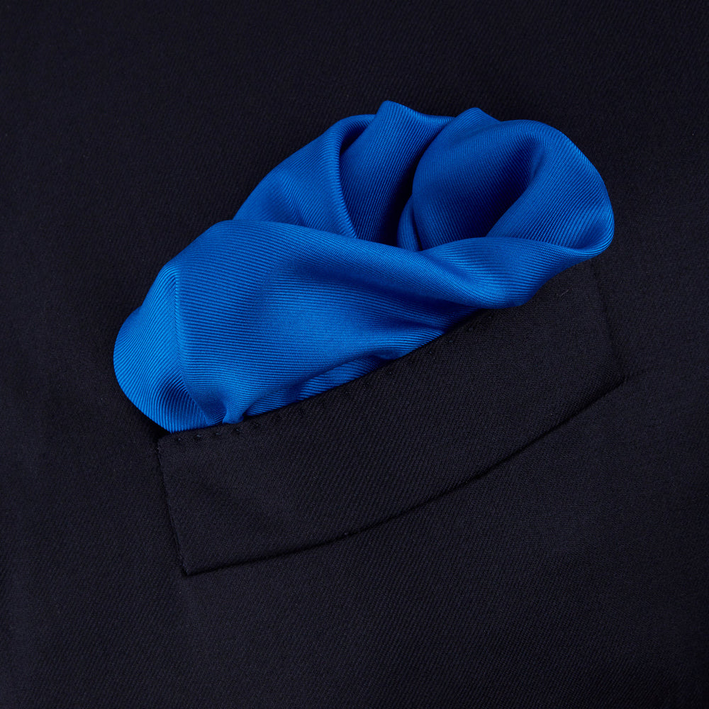 The Royal Blue Piped Silk Pocket Square by Turnbull & Asser features a vibrant blue hue, subtle stitched border, and the brand name printed in white in the lower right corner.