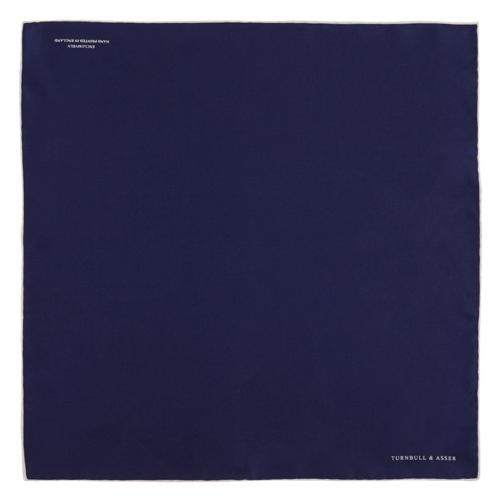 The Navy and White Piped Silk Pocket Square by Turnbull & Asser features white edging and partial corner folding, with the brand’s name printed in white near the lower edge.