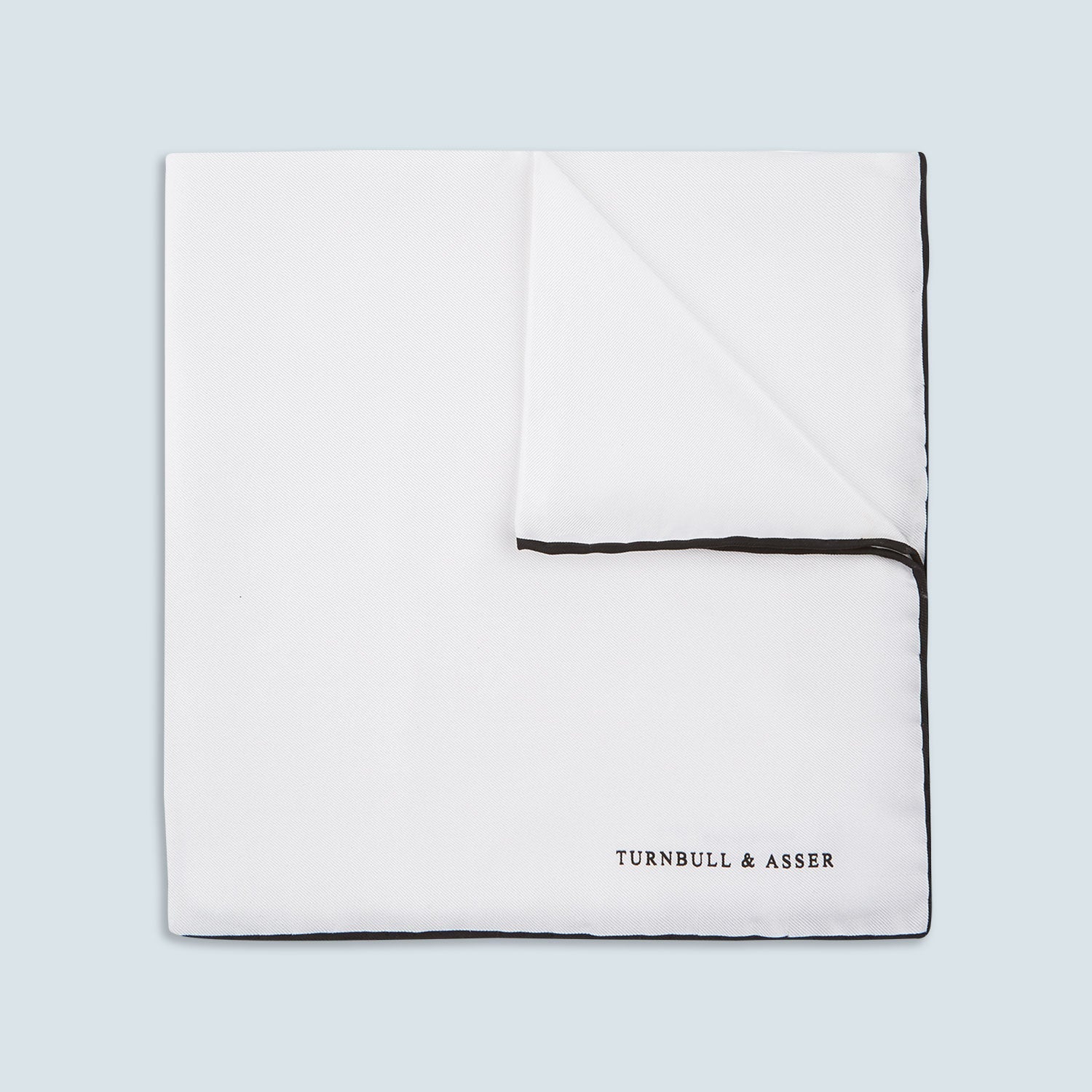 View 1 of product The Turnbull & Asser White and Black Piped Silk Pocket Square features a crisp white base with black edging, neatly folded to showcase the logo in black on the lower right—elegant monochrome style for any occasion, shown on a light gray background.