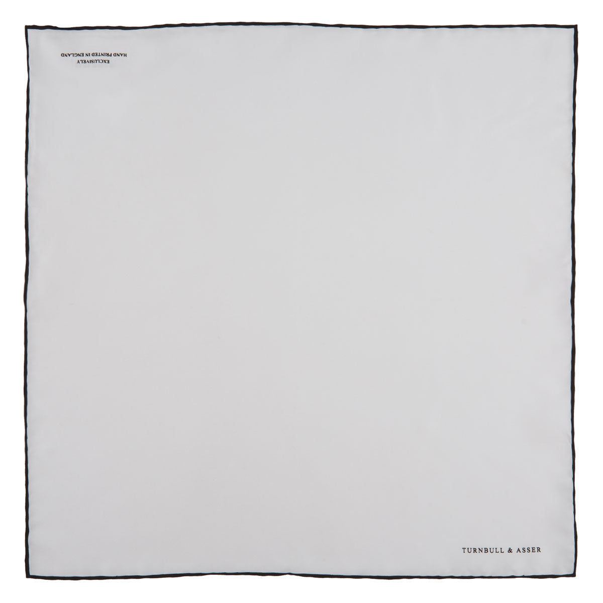 View 2 of product The Turnbull & Asser White and Black Piped Silk Pocket Square features a crisp white base with black edging, neatly folded to showcase the logo in black on the lower right—elegant monochrome style for any occasion, shown on a light gray background.