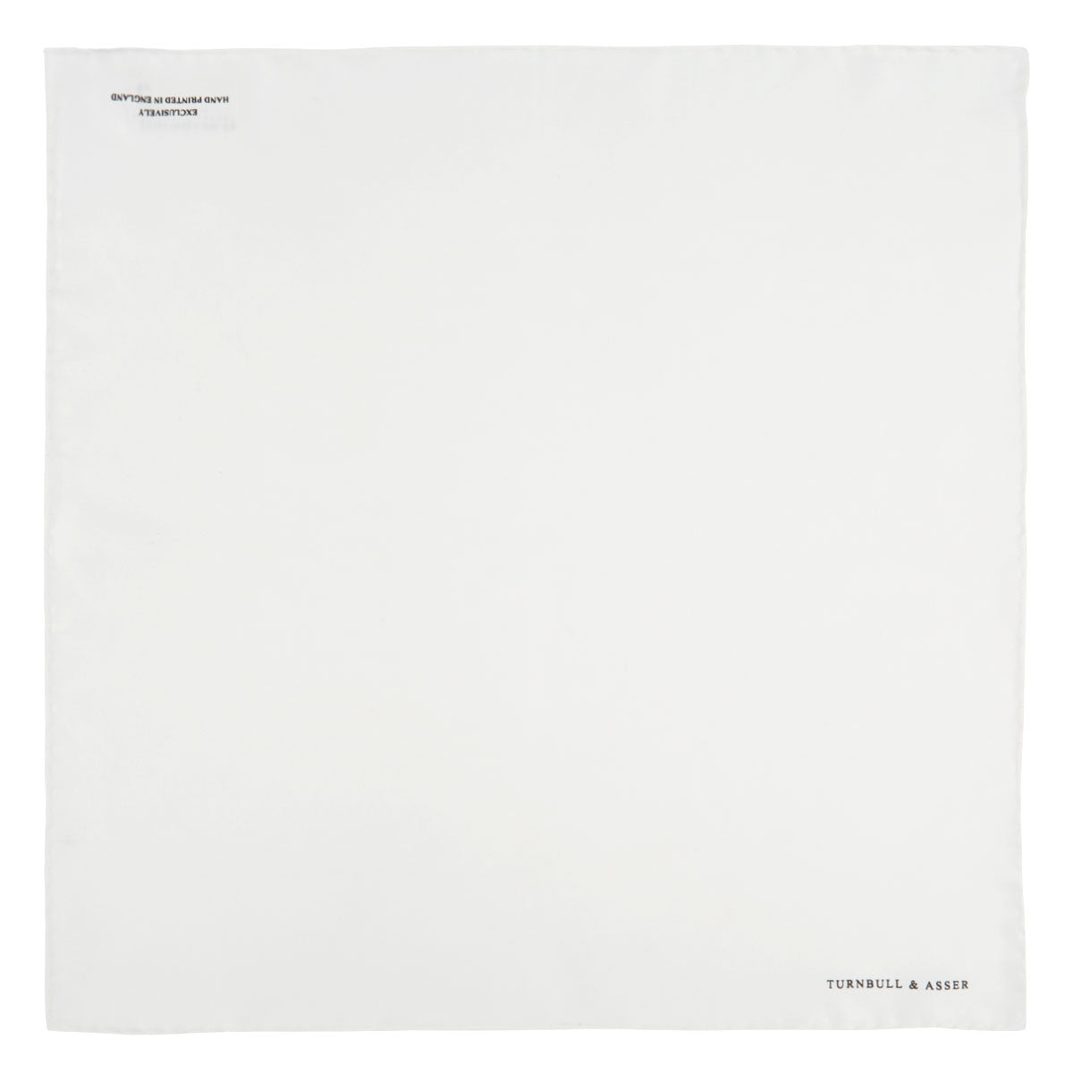 View 2 of product The White Piped Silk Pocket Square by Turnbull & Asser is shown folded at one corner with the brand's logo in black on the lower right, set against a light blue background.