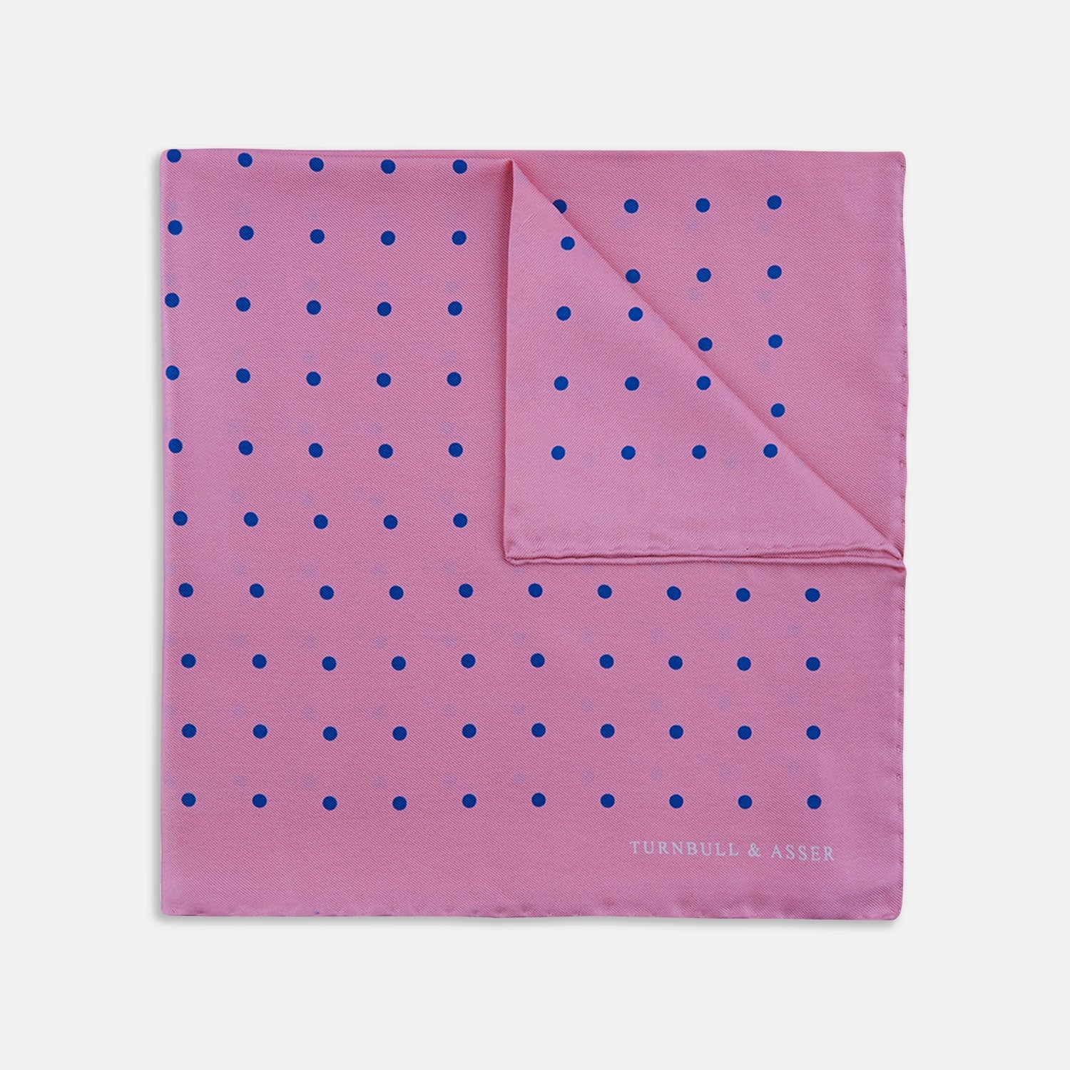 View 1 of product The Turnbull & Asser Rose and Blue Spot Silk Pocket Square features a pastel pink base with evenly spaced blue spots and a discreet white logo in one corner, finished with a slightly folded top for added flair.