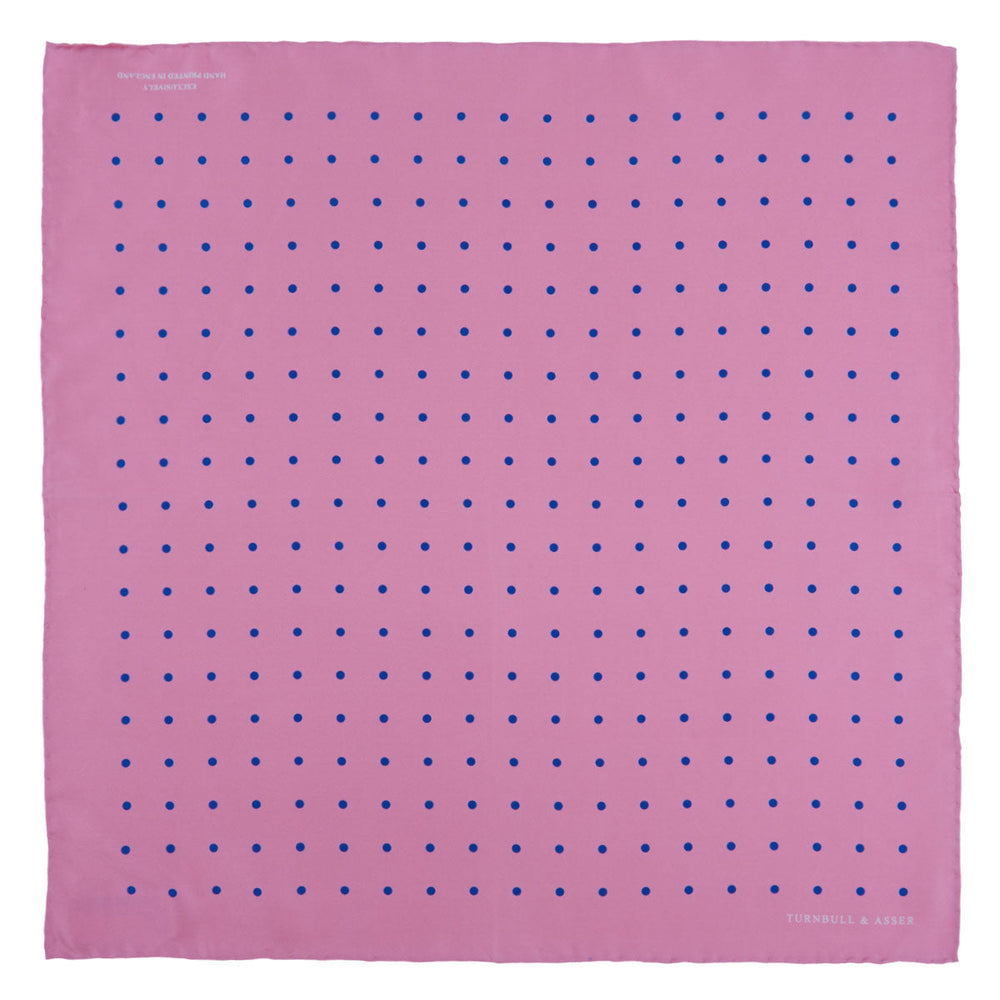 The Turnbull & Asser Rose and Blue Spot Silk Pocket Square features a pastel pink base with evenly spaced blue spots and a discreet white logo in one corner, finished with a slightly folded top for added flair.
