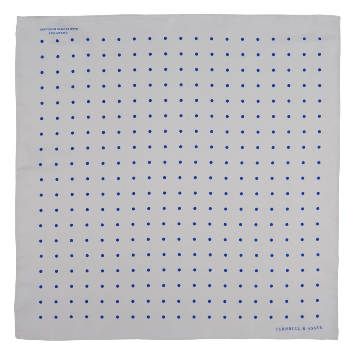 View 2 of product The Turnbull & Asser White and Blue Spot Silk Pocket Square features evenly spaced blue dots, a brand logo in one corner, and is displayed on a light blue background with a stylishly folded corner.
