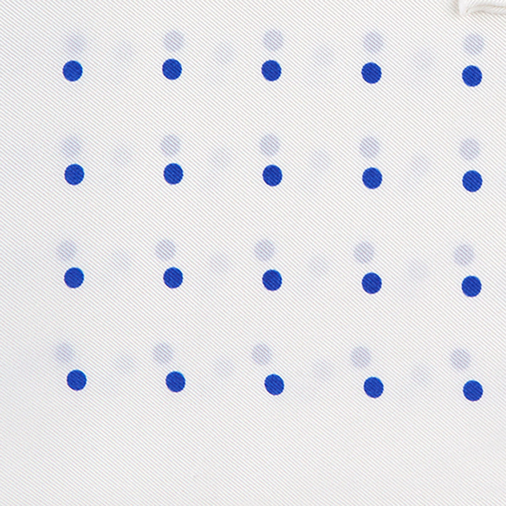 The Turnbull & Asser White and Blue Spot Silk Pocket Square features evenly spaced blue dots, a brand logo in one corner, and is displayed on a light blue background with a stylishly folded corner.