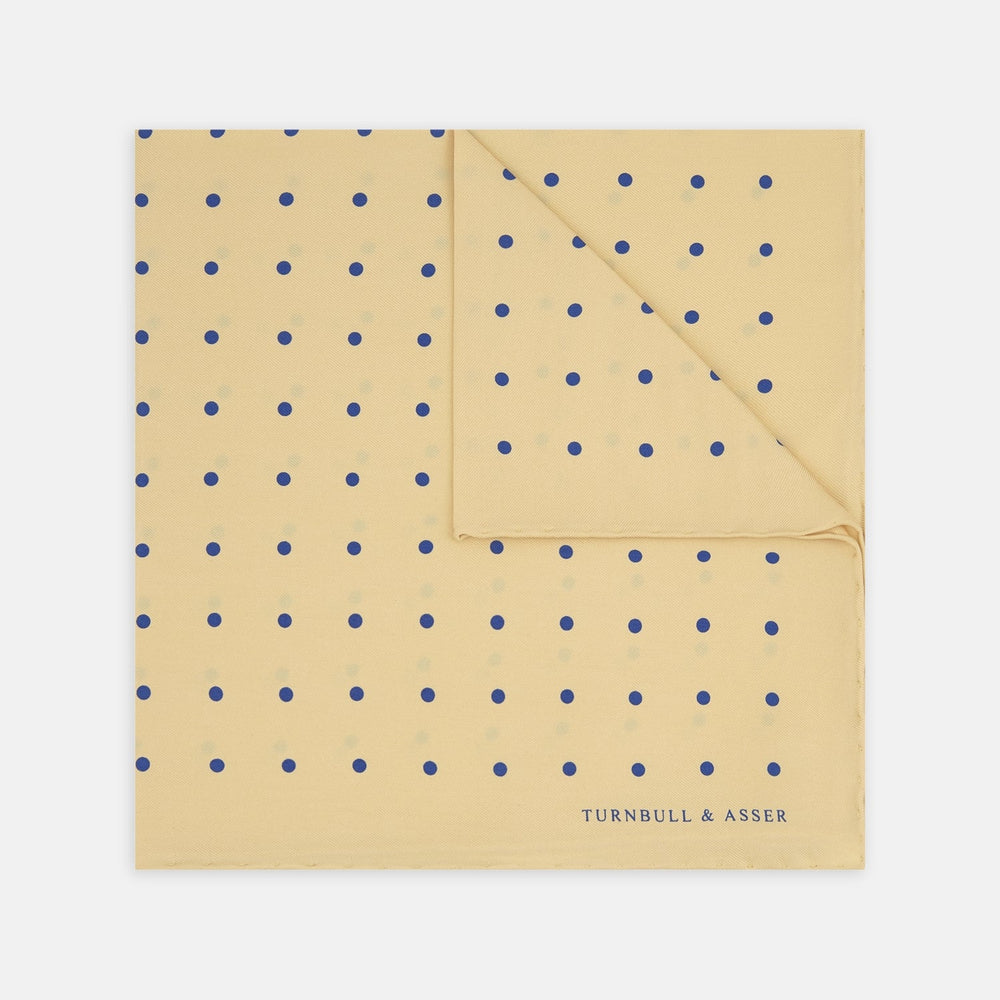 The Yellow and Blue Spot Silk Pocket Square by Turnbull & Asser features evenly spaced blue dots on yellow silk, with the brand name printed in one corner and a refined folded finish.