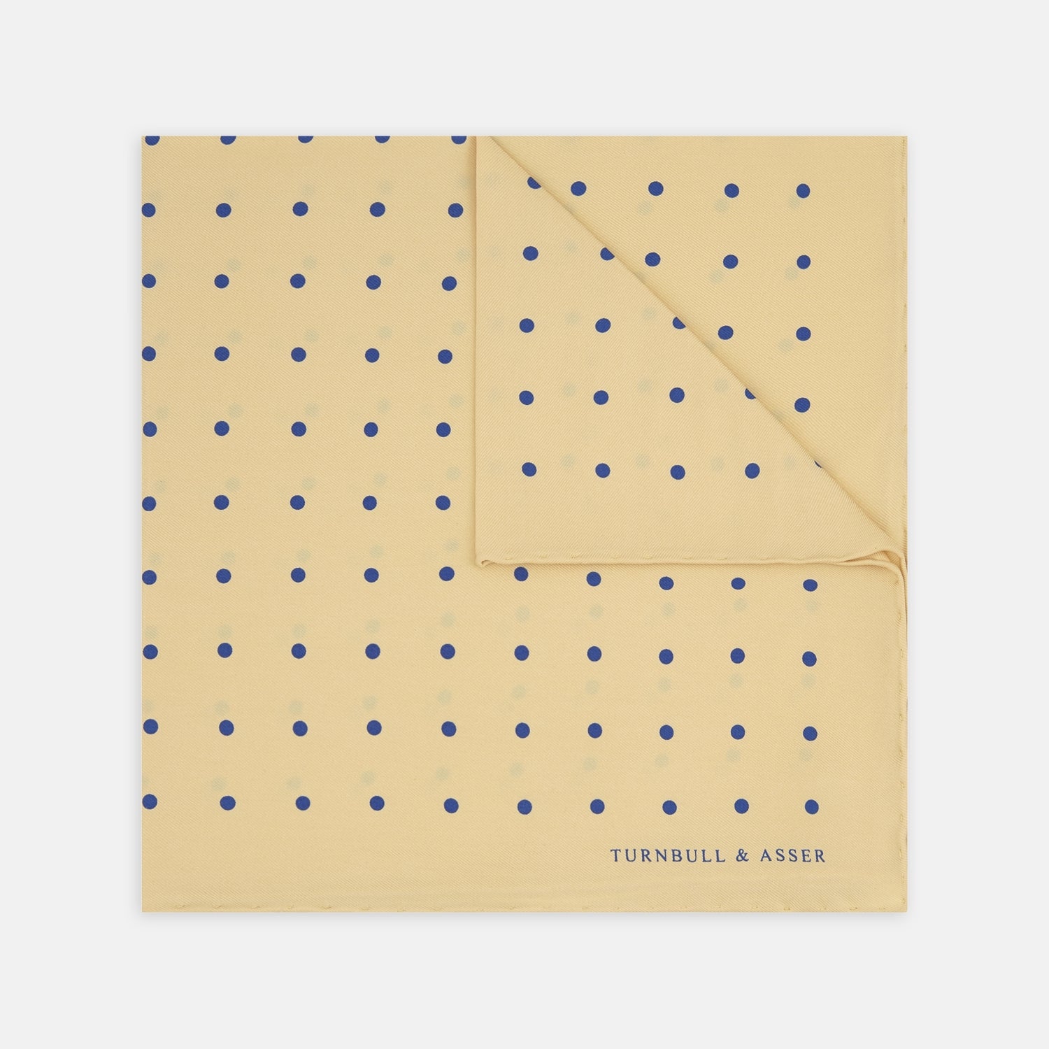 View 1 of product The Yellow and Blue Spot Silk Pocket Square by Turnbull & Asser features evenly spaced blue dots on yellow silk, with the brand name printed in one corner and a refined folded finish.