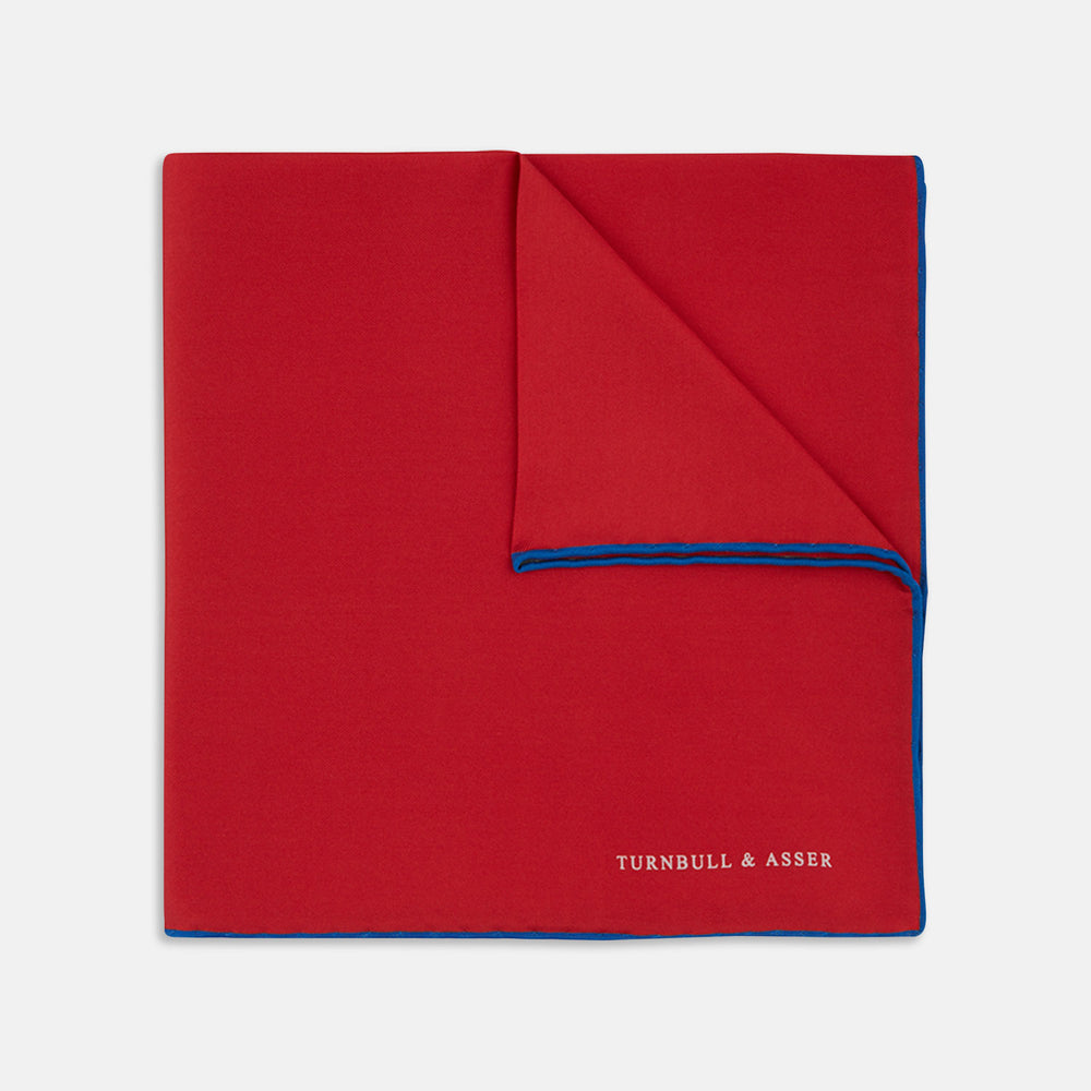 The Red and Navy Piped Silk Pocket Square by Turnbull & Asser features classic red silk with navy edging and the brand’s name printed in white on the bottom right corner.