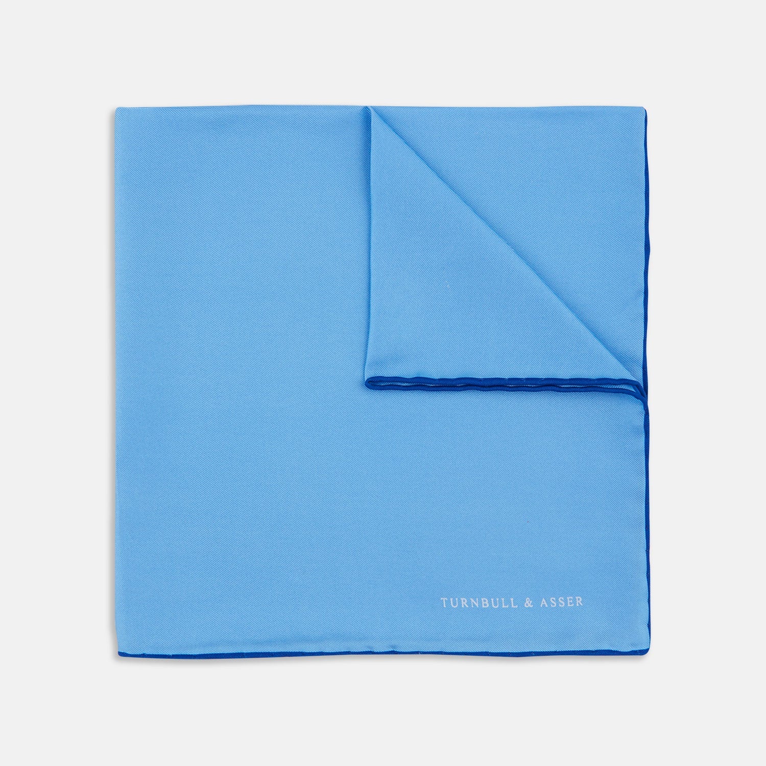 View 1 of product The Light Blue and Navy Piped Silk Pocket Square by Turnbull & Asser, neatly folded with dark blue edges and the brand’s white logo in the corner, is shown on a plain white background—a refined accessory for any occasion.