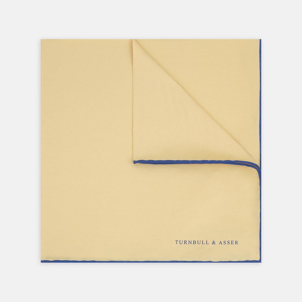 The Yellow and Navy Piped Silk Pocket Square by Turnbull & Asser features blue piping and the brand’s logo in blue on yellow silk—an elegant accessory for any outfit.