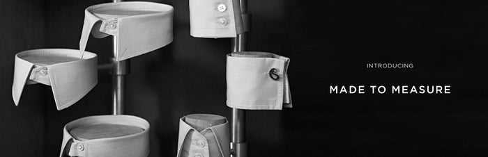 Black and white image of various shirt collars and cuffs displayed vertically on rods, with the text Introducing Made to Measure on the right side against a dark background.