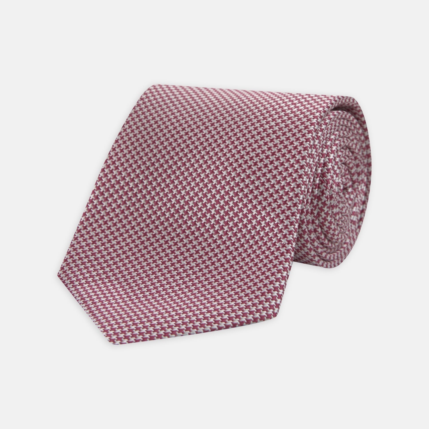View 1 of product The Turnbull & Asser Dark Pink Houndstooth Silk Tie is rolled up and displayed on a plain white background.