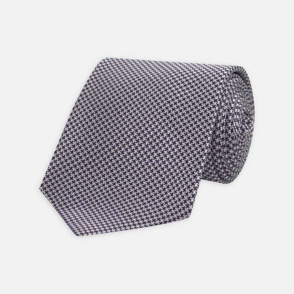 The Plum Houndstooth Silk Tie by Turnbull & Asser features a refined small black, white, and gray pattern—perfect as an office shirt accessory—shown rolled up on a plain white background.