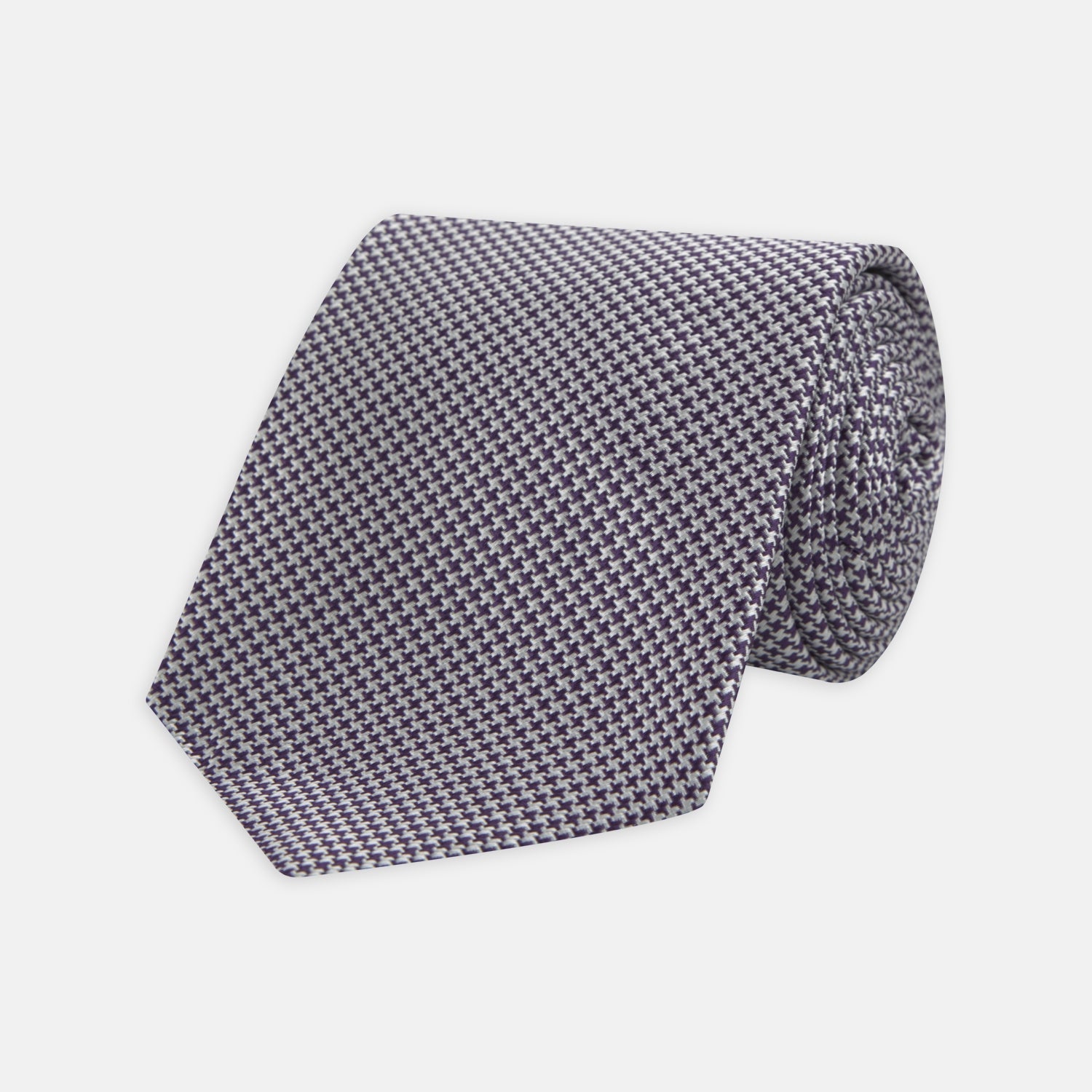 View 1 of product The Plum Houndstooth Silk Tie by Turnbull & Asser features a refined small black, white, and gray pattern—perfect as an office shirt accessory—shown rolled up on a plain white background.