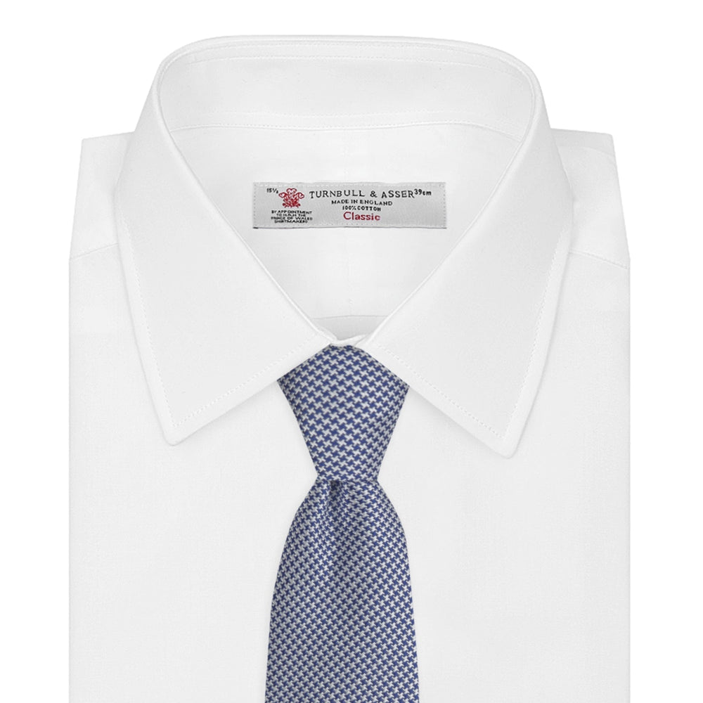 The Turnbull & Asser Blue Houndstooth Silk Tie features a classic blue and white pattern, rolled and displayed on a white background—an elegant accessory for your favorite office shirt.